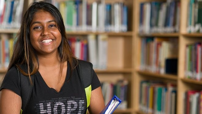 Young woman smiling in front of library shelves