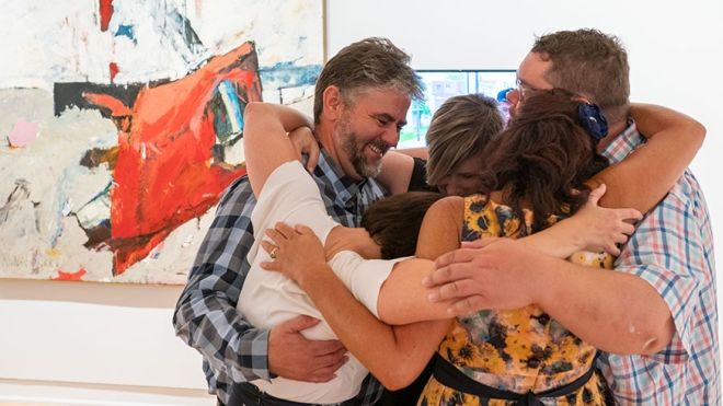Group of adults hugging and smiling in an art gallery
