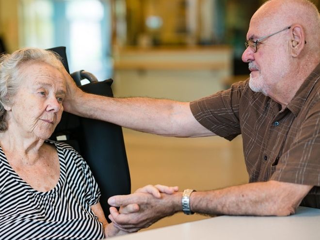 Middle aged man holding hands with and comforting a senior woman